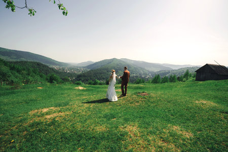 Happy stylish couple newlyweds in the green forest on summer day. bride in long white dress and...
