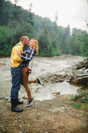 Couple in love - young hipster man is carrying his redhead woman on back near the river in the mountain.の写真素材