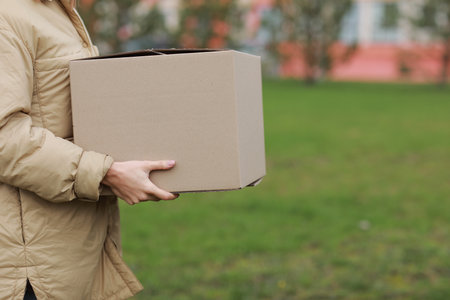 Delivery woman in a red Santa Claus hat and medical protective mask holds a big box outdoor. New Year's Christmas parcel in box, delivery online store in Quarantine time. Service coronavirusの写真素材