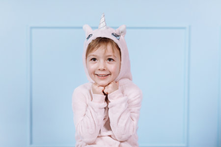 Smiling beautiful little girl in unicorn pink costume is smiling and having fun with disco ball on a blue wall background. happy childhoodの写真素材