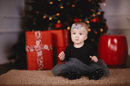 cute baby girl in dress and bow on head on bed with Christmas background behindの写真素材