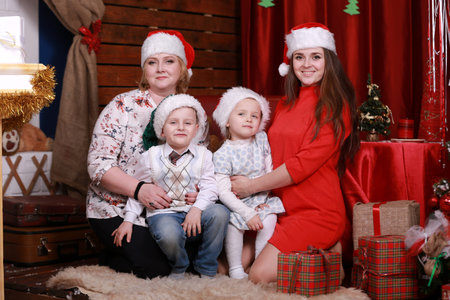 Happy family posing for photo at christmas. grandmother and mother with two children in santa hats.