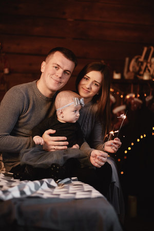 cute young family dad, mom and baby girl with sparklers on bed with Christmas background behindの写真素材
