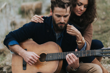 caucasian man is playing guitar with woman by the lake. Young couple is hugging on autumn day outdoors. A bearded man and curly woman in love. Valentine's Day. Concept of love and familyの写真素材