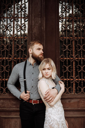 Beautiful, cheerful and lively newlyweds, groom and bride are hugging near the blooming pink cherry blossom. Wedding portrait of a close-up of a smiling bearded groom and a cute brideの写真素材