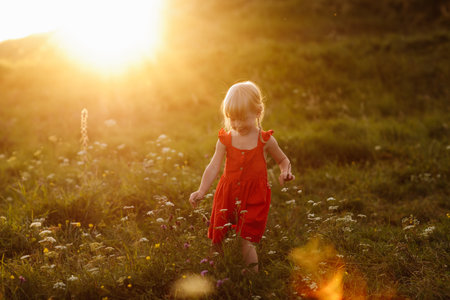 Portrait of a little beautiful girl in red dress on nature on summer day vacation. The playing in the green field at the sunset time. Close Up. The concept of family holiday and time togetherの写真素材