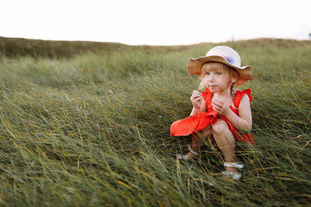 Portrait of a little beautiful girl in red dress on nature on summer day vacation. The playing in the green field at the sunset time. Close Up. The concept of family holiday and time togetherの写真素材
