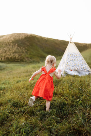Portrait of a little beautiful girl in red dress on nature on summer day vacation. The playing in the green field at the sunset time. Close Up. The concept of family holiday and time togetherの写真素材