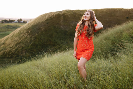 Portrait of a beautiful woman in red dress in green grass on field, nature on summer day vacation....