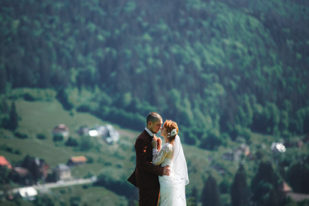 Happy stylish couple newlyweds in the green forest on summer day. bride in long white dress and groom in red suit are hugging. wedding dayの写真素材