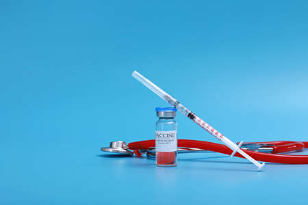 Medicine bottle with coronavirus vaccine covid-19. Medical glass vial, stethoscope and syringe for vaccination. liquid vaccine in laboratory, hospital or pharmacy concept isolated on blue background.の写真素材