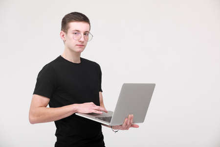Distance learning online education. portrait of a young man in a black T-shirt with glasses with a laptop on a white background. copy space.の写真素材