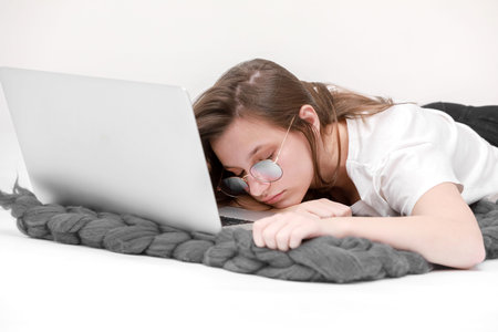 Portrait of a beautiful young girl with blond hair in glasses and a white T-shirt working or...
