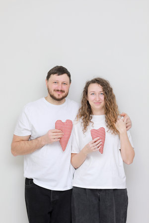 valentines day. young smily man and woman in white t-shirts with red hearts in their hands. couple...