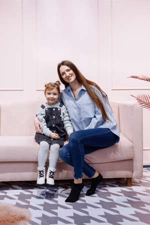 mother's day. Portrait of little preschool girl kid excited young mother have fun playing together at studio, happy mom and daughter hug cuddle show love, enjoy family relaxing weekend on pink sofa.の写真素材