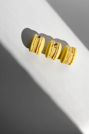 three sweet yellow lemon french macaroons or macarons dessert isolated on white background with light rays from window.の写真素材