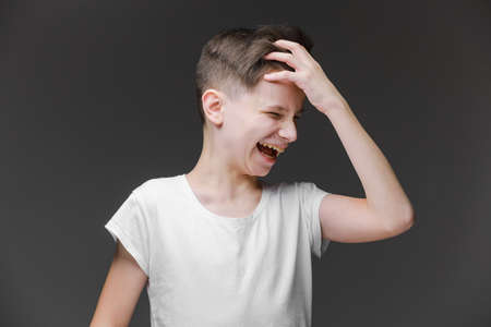 Teenager boy wearing white t-shirt standing on gray background smiling with tongue out showing fingers of both hands doing victory sign. out happy with funny expression. Emotion concept.Number twoの写真素材