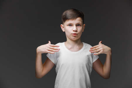 Teenager boy wearing white t-shirt standing on gray background smiling with tongue out showing fingers of both hands doing victory sign. out happy with funny expression. Emotion concept.Number twoの写真素材