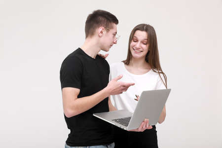 Portrait of a smiling teens boy and girl holding laptop computer while standing and looking in it isolated over white wall background. Study and workの写真素材