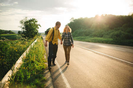 A man and a woman are hitchhiking. A young couple goes hitchhiking around the country. Free hitchhiking trip. A lover who travels free by hitchhiking. The couple goes traveling. Couple by the road.の写真素材