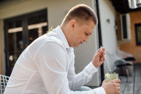 Man relaxing and drinking mohito in cafe on terrace. Summer day. smiling and enjoying Dragonfly on the shoulder.の写真素材