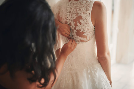 Bridesmaid helping bride fasten corset close-up and getting her dress, preparation concept in...