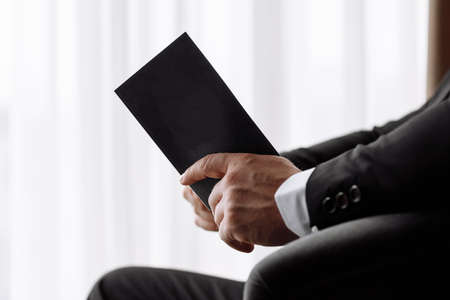 the groom holds an envelope with a letter from the bride. man is reading and sitting in the chair near the window. A letter for the groom. declaration of loveの写真素材