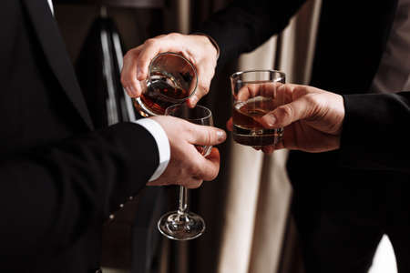 Business meeting. Men hold glasses of whiskey. Men's Party. Hand with a drink of alcohol.の写真素材