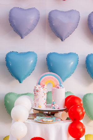 big Birthday cake with rainbow, colorful Sprinkles. on many colorful heart balloons background. birthday party.の写真素材