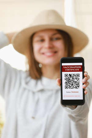 A defocused young girl is holding a passport and a smart phone with a certificate of vaccination against the  disease. focus on the smart phone. Health Passport concept.の写真素材