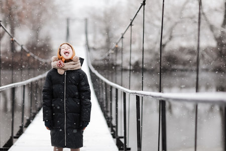 Funny little girl catches snowflakes in a beautiful winter park during a snowfall. Cute baby is playing in the snow. Winter activities for children. the winter holidays. happy childhoodの写真素材