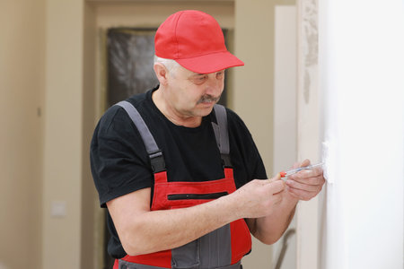 Man in work overalls using wrench while installing heating radiator in room. plumber installing...