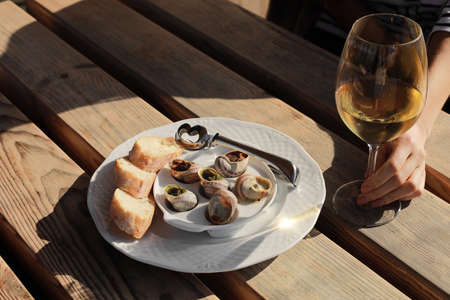 Girl sitting in outdoor cafe enjoying escargot snails with herbs butter and white wine.の写真素材