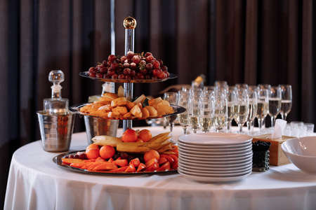 Wedding day reception. Buffet table. Catering service. Plates with berries, raspberry, blackberry. Delicious gourmet food for guests.Many glasses, bottles of champagne, wine.の写真素材