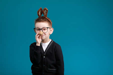 Cheerful boy in rabbit bunny ears on head on blue studio background. Excited crazy smiling happy child in glasses. Easter blue color of the year painting eggs in hands. Easter and holidays.の写真素材