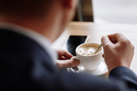 A man in a business suit holds a cup of hot coffee in his hands. Morning businessman in cafe .Copy...