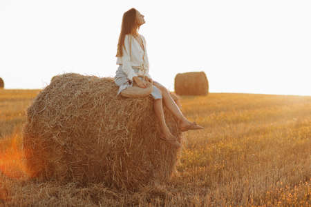 beautiful young woman with long hair and straw bag in hand in the summer at sunset in the field for a walk. she is happy. background blurred art photography. summer holiday conceptの写真素材