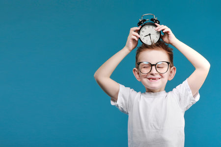 Little boy taking a picture using a retro camera and with finger pointed up. Child boy with vintage photo camera isolated on blue background. Old technology concept. Child learning photography.の写真素材