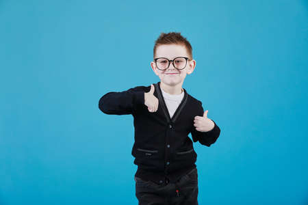 Little boy taking a picture using a retro camera and with finger pointed up. Child boy with vintage photo camera isolated on blue background. Old technology concept. Child learning photography.の写真素材
