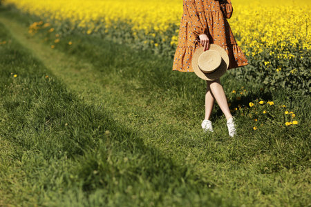 cropped photo of young woman walks in a field of yellow rapeseed. Girl brunette long hair fly in...