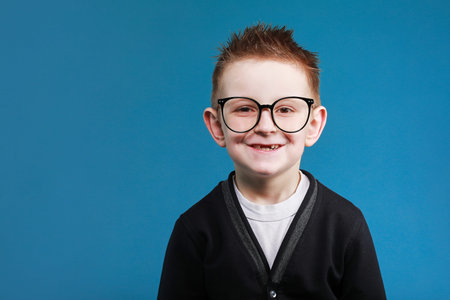 Like. Portrait of happy little schoolboy with glasses smiling at camera and doing thumbs up gesture,...