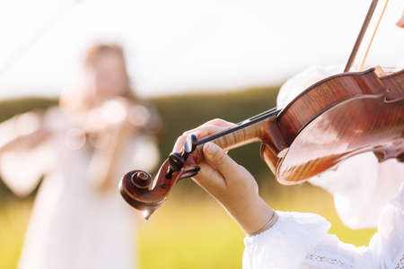 little girl is playing violin outdoor with garden in the background on sunny summer day. Image with selective focus and copy spaceの写真素材