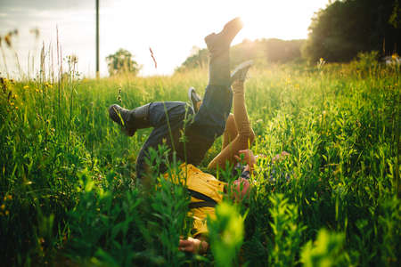 woman and man having fun outdoors. Loving hipster couple walking in the field, kissing and holding hands, hugging, lying in the grass and lifting their legs up in the summer at sunset. valentines day.の写真素材