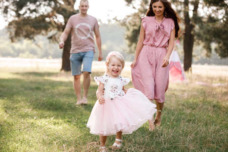View on toddler. Mother, father with daughter enjoy nature and walk in the park. Young family spending time together on vacation, outdoors. The concept of family summer holidayの写真素材