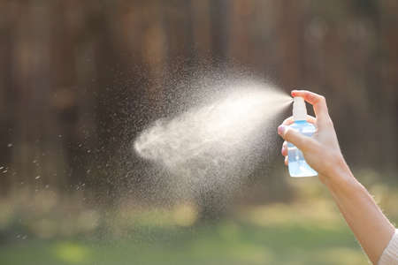 Woman hand holding a bottle and spraying on nature background. antiseptic, mosquito repellent, freshening the air.の写真素材