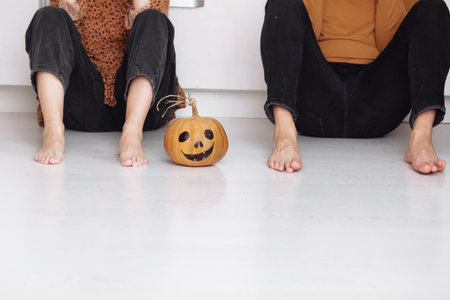 Crop view of young man and woman sitting on the floor at home with halloween pumpkin. pumpkin...