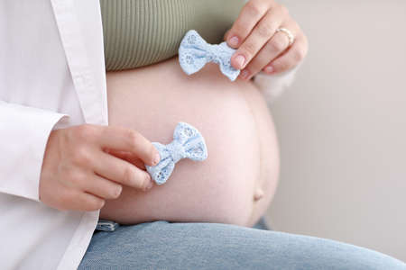 close up hands on pregnant mother holding baby clothes, two blue bows. Lover woman waiting child. Preparation for childbirth, Girl big belly advanced pregnancy.の写真素材