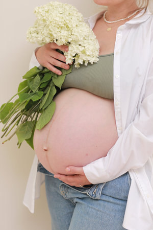 healthy pregnancy. Side view pregnant woman with big belly advanced pregnancy in hands. girl holding big bouquet of flower. copy space for text. Elegant mother waiting baby.の写真素材