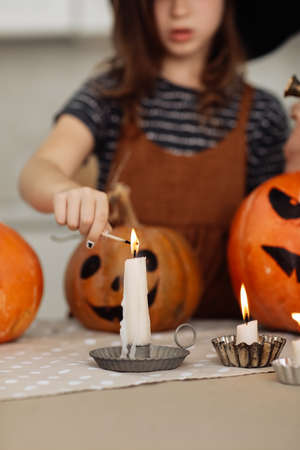 child girl lights a candle for Halloween. little girl in witch costume with carving pumpkin with a face made by child. Happy family preparing for Halloween. selective focus.の写真素材