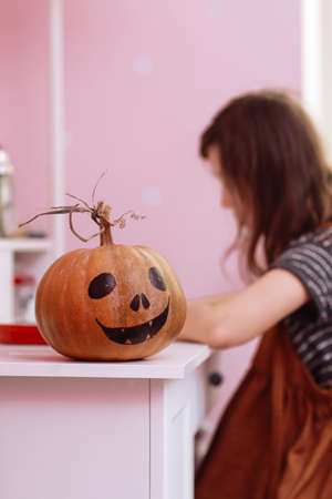 Halloween pumpkin on wooden table in schoolgirls room. child girl on backgroung doing homework.の写真素材